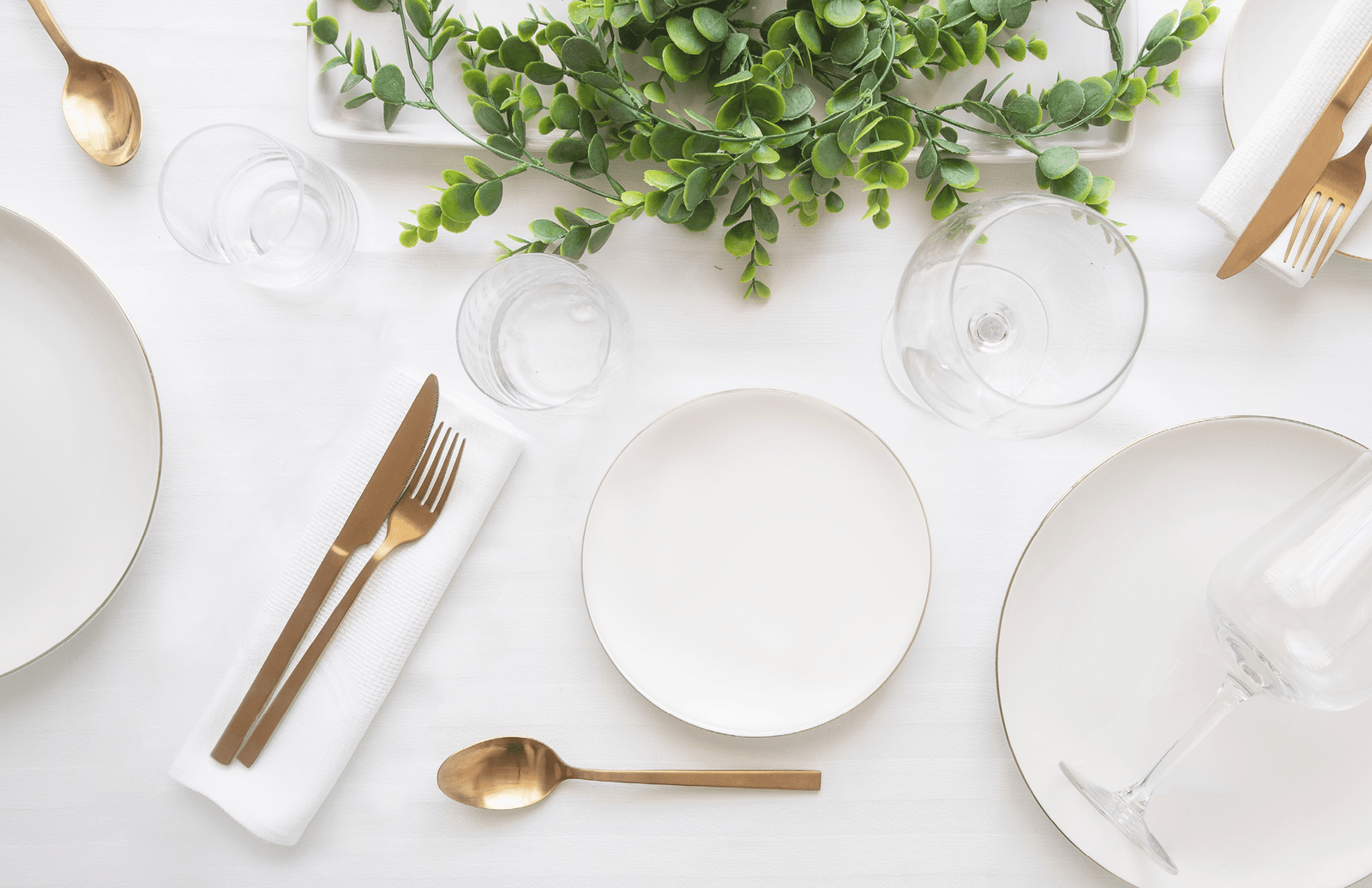 Tableware background in white gold tone.White plates, gold cutlery,  wine glasses and decorative plant centrepiece