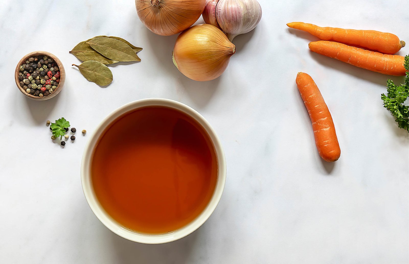 Flat lay of homemade beef bone broth in a bowl with ingredients. Contains minerals and healthy nutrients, including vitamins, amino acids, and essential fatty acids. 